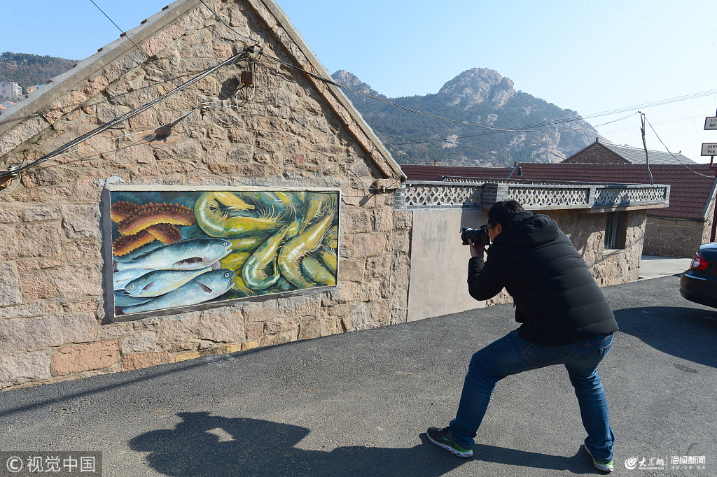 省荣成市石岛管理区港湾街道牧云庵村,媒体记者正在拍摄渔民作墙画